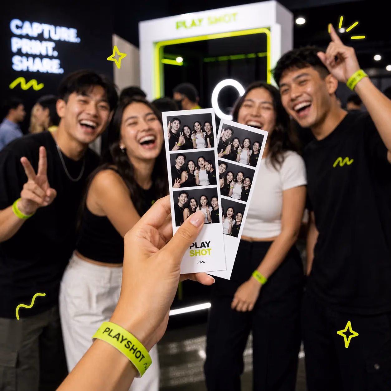 Four friends laughing at a PlayShot booth, one holding up their printed photo strip